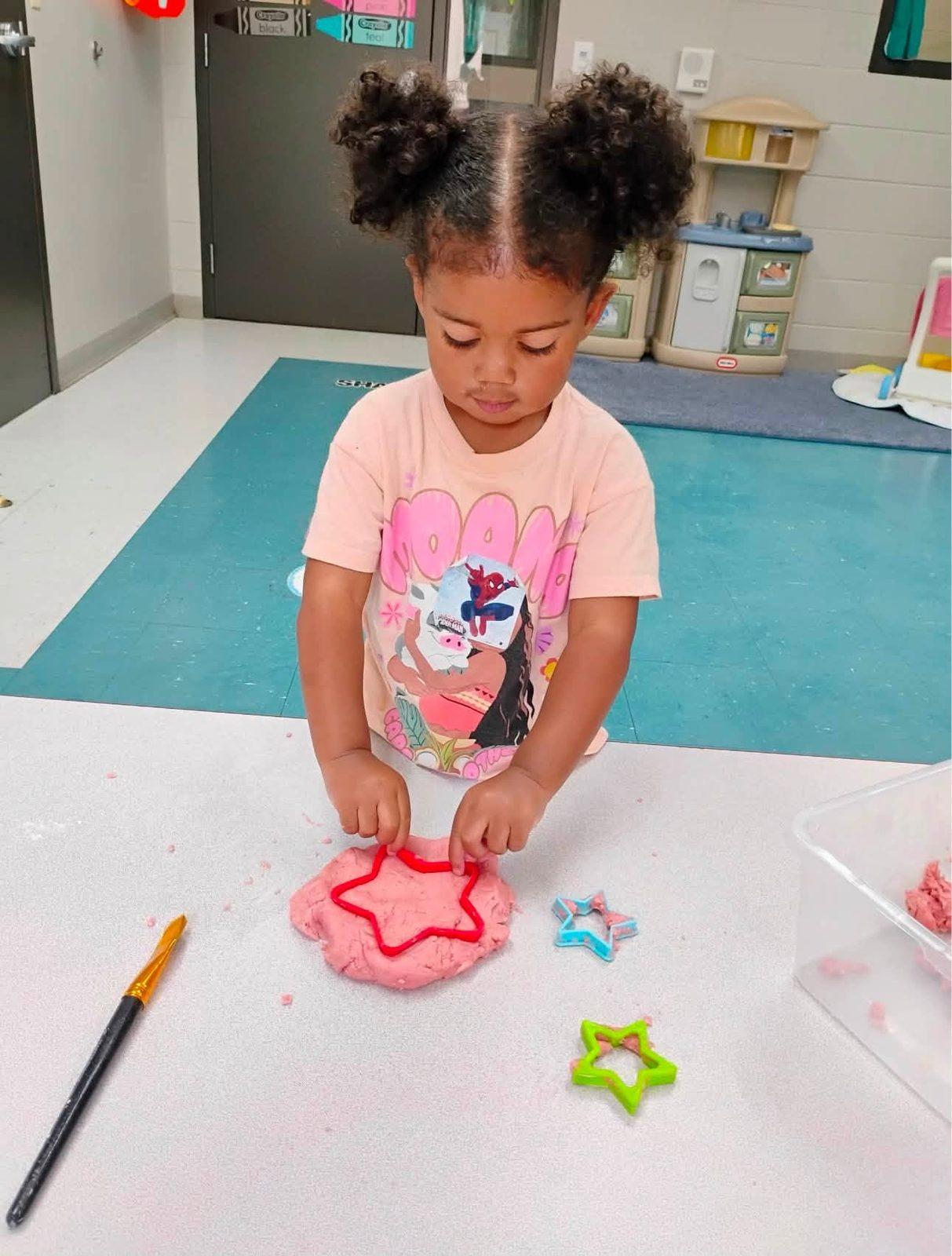 Preschooler pressing cookie cutters into pink play dough
