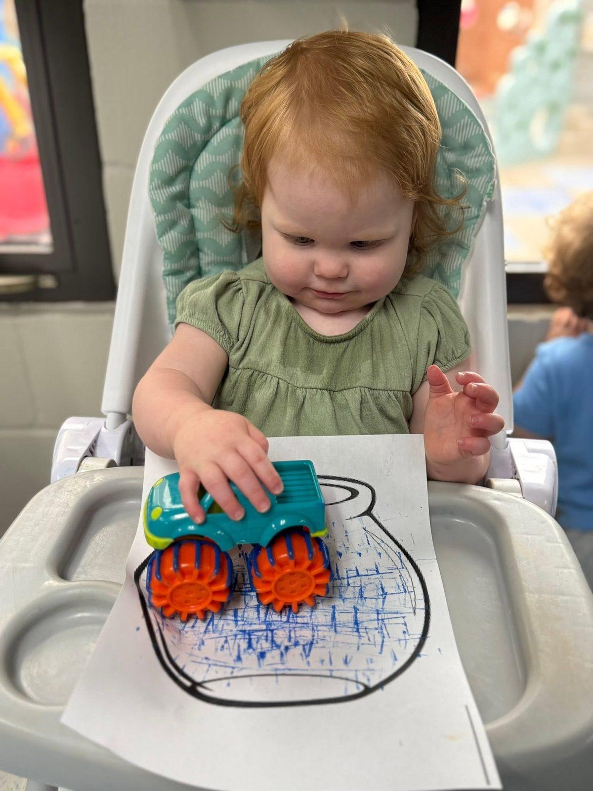 Toddler painting with a toy truck in a high chair