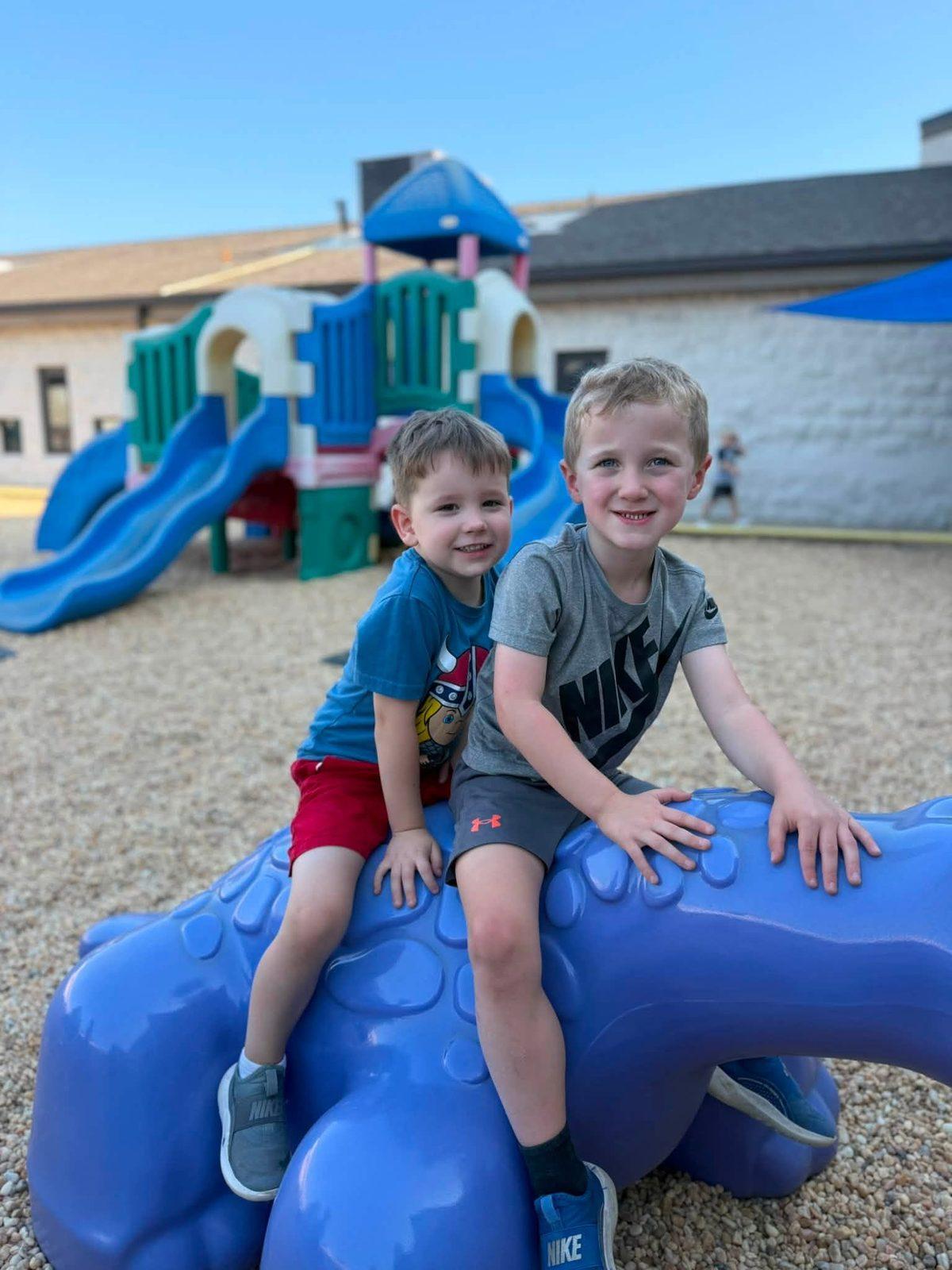 Two boys sitting on a playground dinosaur