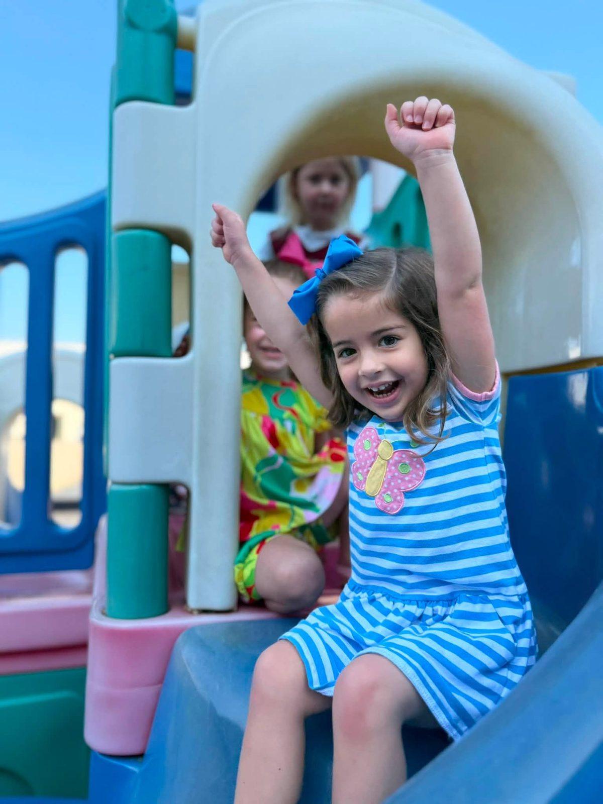 KCCDC student cheering at the top of the playground slide